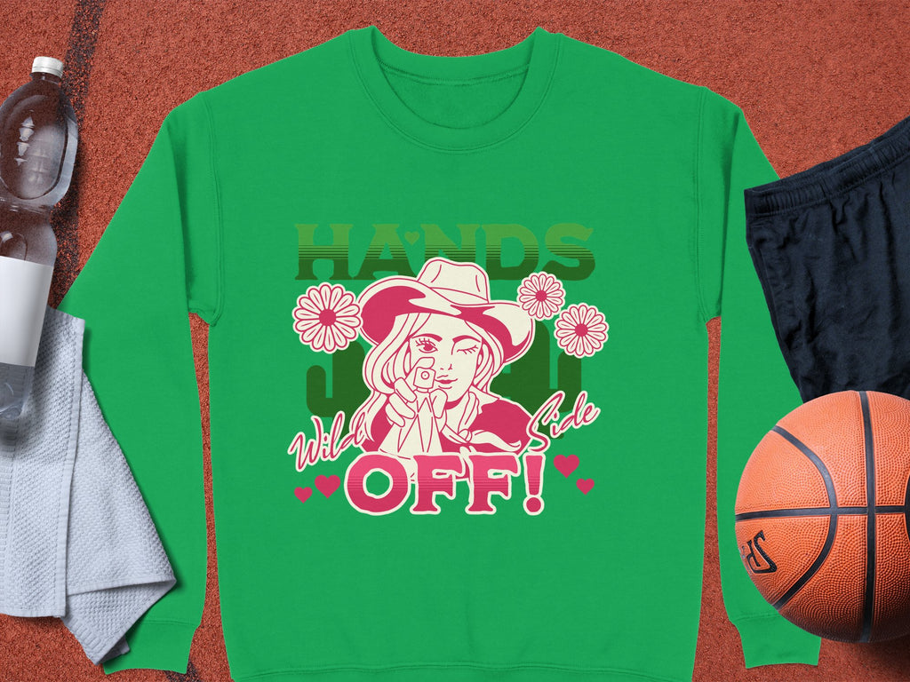Explore Garment Graphics Wild Side Sweatshirts. This green sweatshirt showcases a person with a toy gun, cowboy hat, surrounded by flowers, and marked with Hands Wild West Sale OFF! and hearts. Pair it with essentials like a towel, water bottle, black shorts, and a basketball.