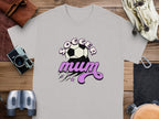A light gray, classic fit T-shirt by Garment Graphics featuring a Soccer mum design with a soccer ball and pink accents is placed on wood. Nearby are a camera, binoculars, leather pouch, and gloves.