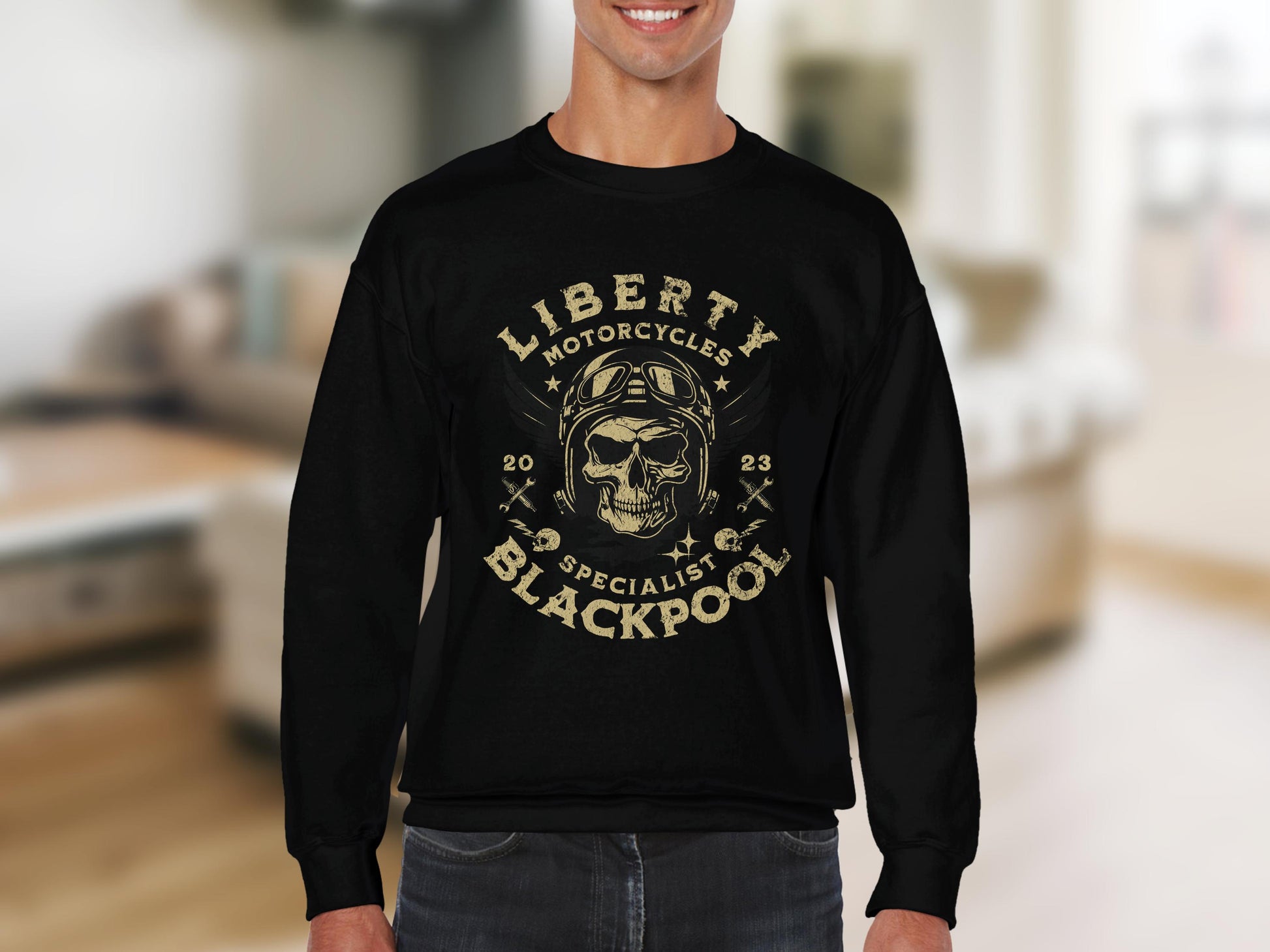 Someone is wearing a black long-sleeve shirt by Garment Graphics, featuring a skull with goggles and a helmet design. The text reads Liberty Motorcycle Specialist Blackpool 2023 against a blurred indoor background.