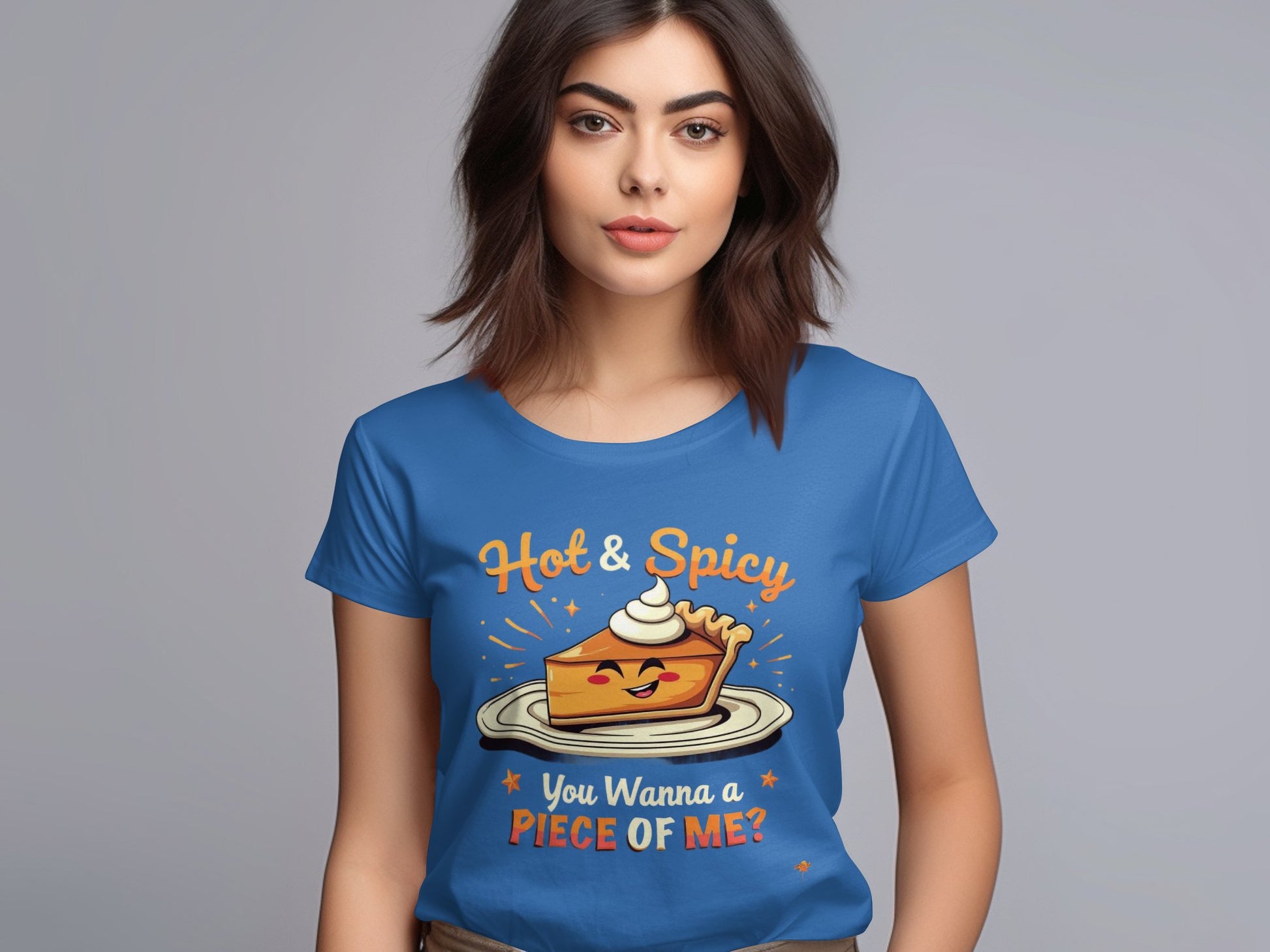 A brown-haired woman wears a Garment Graphics T-shirt, ideal for casual outings. The design shows a pie slice with eyes, cream on top, and the text Hot & Spicy, You Wanna a Piece of Me? in womens sizing against a plain gray background.