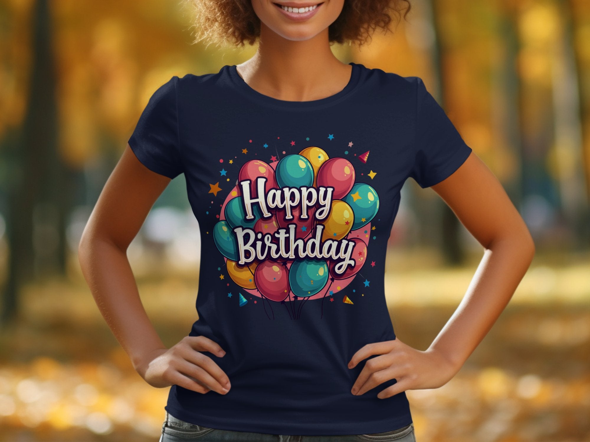 A person stands outside in a vibrant Garment Graphics navy blue T-shirt, featuring colorful balloons and Happy Birthday amidst stars. Made from 100% cotton, it perfectly embodies the birthday celebration theme against a backdrop of blurred autumn trees.