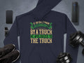 A humorous Garment Graphics hoodie with If an Englishman gets run down by a truck he apologizes to the truck rests on gray. Nearby, essentials like black sneakers, a smartphone, smartwatch, wireless speaker, and adjustable dumbbells add flair to English etiquette.