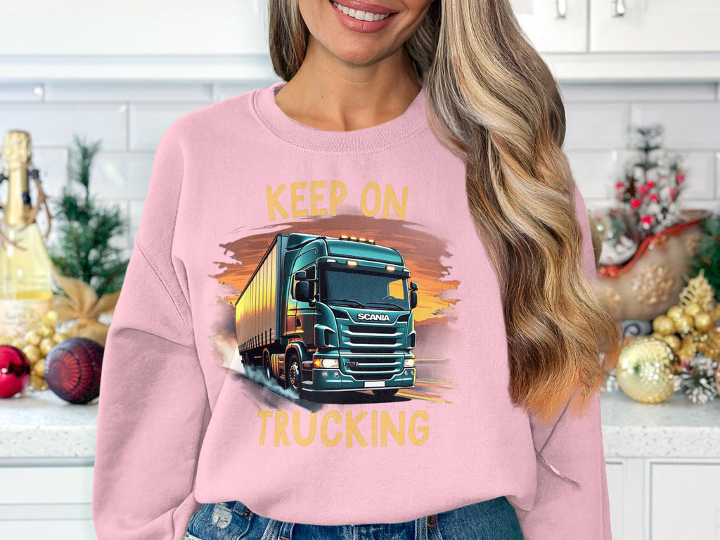 A long-haired individual stands in a kitchen, showcasing their love for trucks by wearing a Garment Graphics sweatshirt that reads Keep on Trucking. Festive ornaments and a small Christmas tree add to the cheerful backdrop.