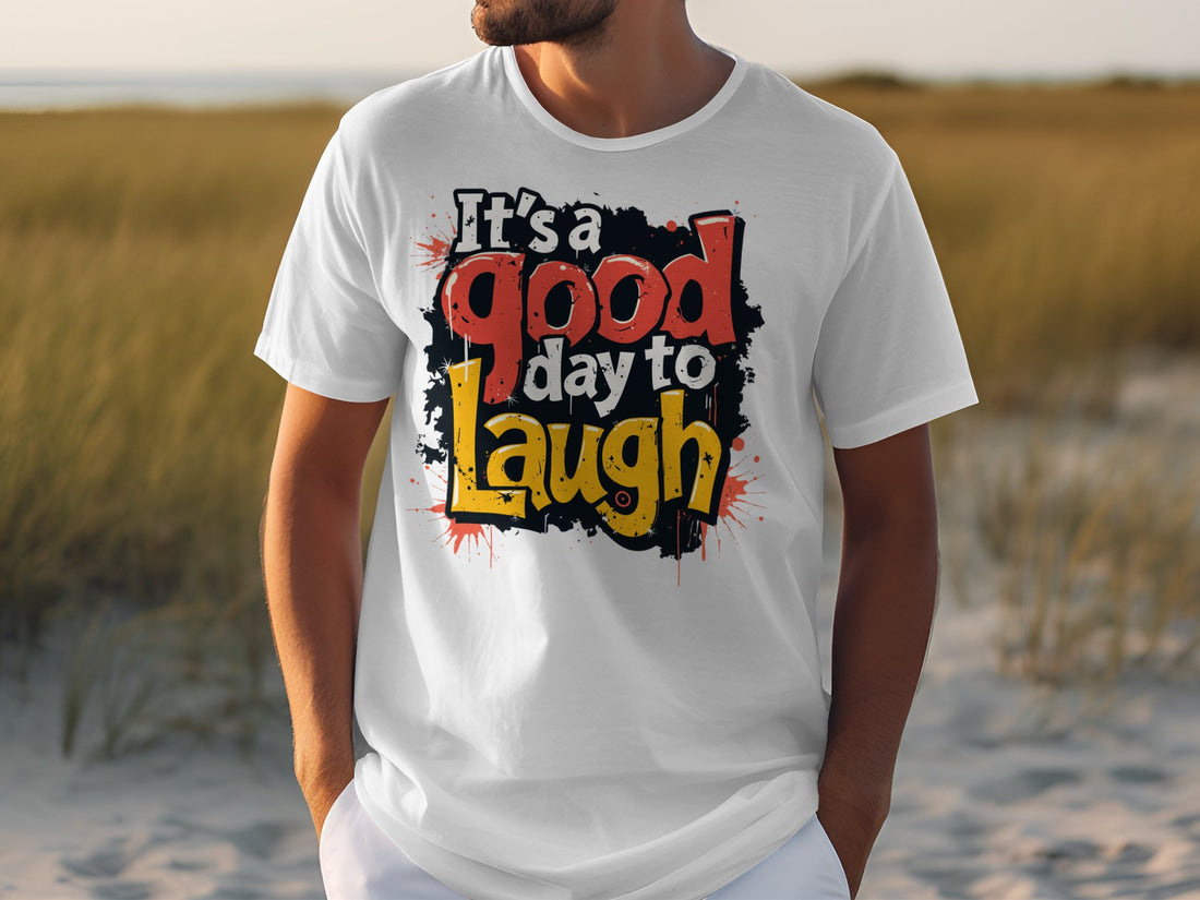 Wearing a Garment Graphics Its a Good Day to Laugh T-shirt, a person casually stands with hands in pockets. The shirts vibrant colors amplify the relaxed, outdoor vibe against sandy beach and grassy dunes.