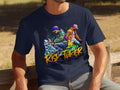 A man wears a Garment Graphics dark blue t-shirt adorned with lively graffiti art of two dancers and the phrase Risk Taker, Street Dance with Friends. Set against a grassy backdrop, this piece honors street dance culture.
