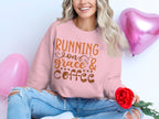 A person sits cross-legged in a Garment Graphics pink graphic sweatshirt with Running on Grace & Coffee in unisex sizing. Holding a red rose, theyre surrounded by pink heart-shaped balloons, their long wavy hair cascading over ripped jeans.
