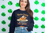 A woman models a Garment Graphics unisex navy sweatshirt featuring a pie graphic with the text Hot & Spicy, You Wanna A Piece Of Me? against green four-leaf clovers, styled with denim shorts for bold comfort.