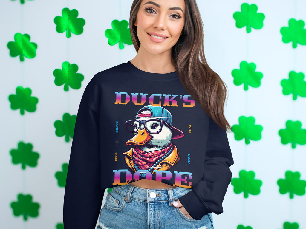 A person stands before a wall adorned with green shamrocks, showcasing a bold fashion statement in Garment Graphics trendy cartoon sweatshirt. It depicts a duck with glasses, a hat, and a scarf, with Ducks Dope written prominently.