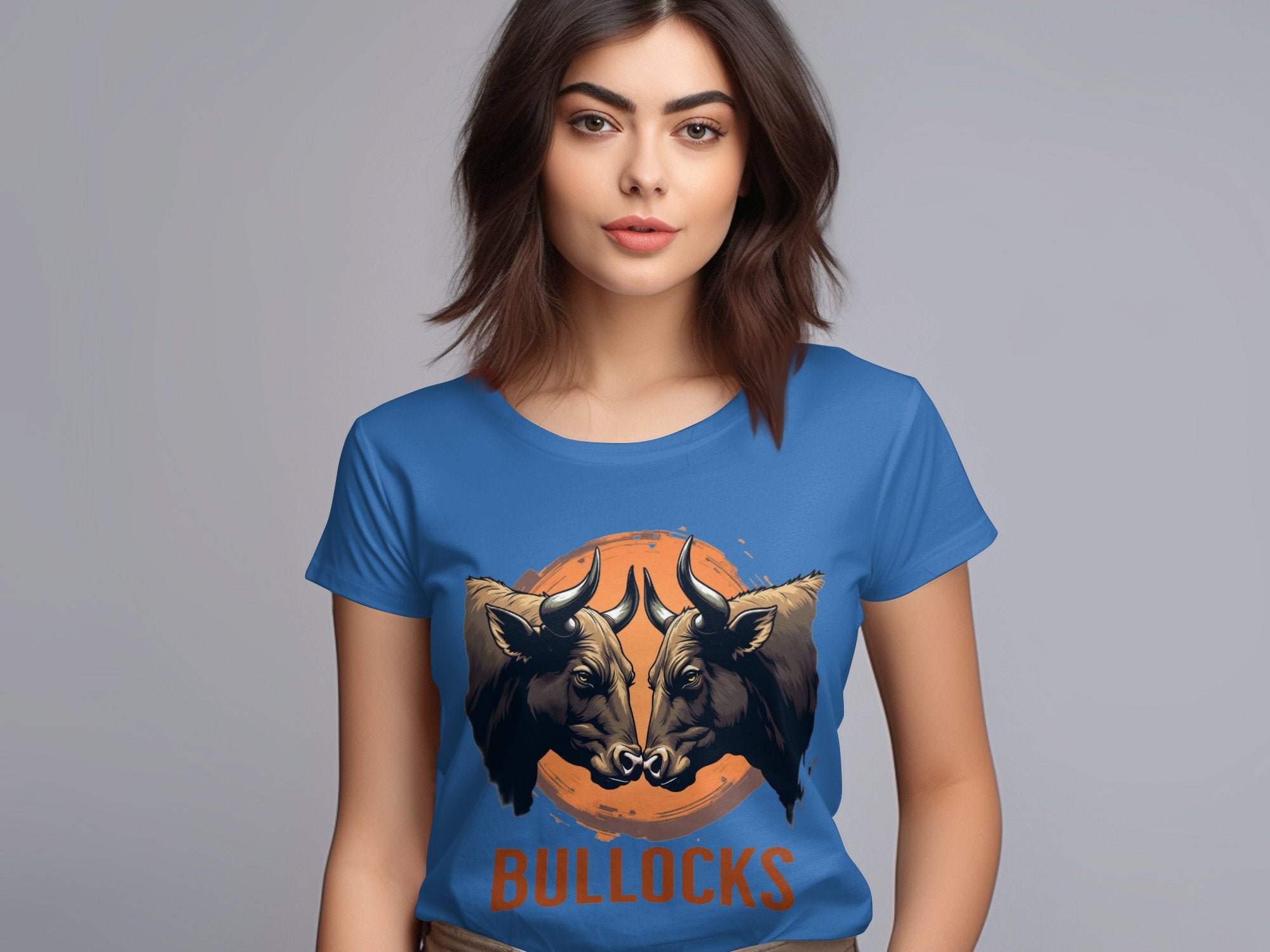 A woman wears a Garment Graphics T-shirt featuring striking graphics: two bulls facing each other over an orange circle, with BULLOCKS printed below on a plain gray background.