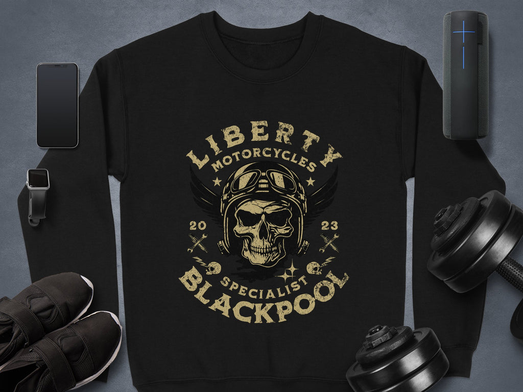 Garment Graphics offers a stylish black sweatshirt showcasing a skull with goggles and a helmet, encircled by Liberty Motorcycles Specialist Blackpool 2023. Essentials like a phone, smartwatch, shoes, dumbbells, and portable speaker complete the perfect Blackpool 2023 collection.