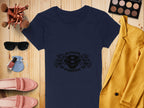 A flat lay image highlights a Garment Graphics navy T-shirt with Scania V8 Power design, paired with a yellow blazer, pink shoes, sunglasses, and a blue purse. Completing the look are makeup brushes, an eyeshadow palette with eagle heads, and nail polish on a wooden surface.