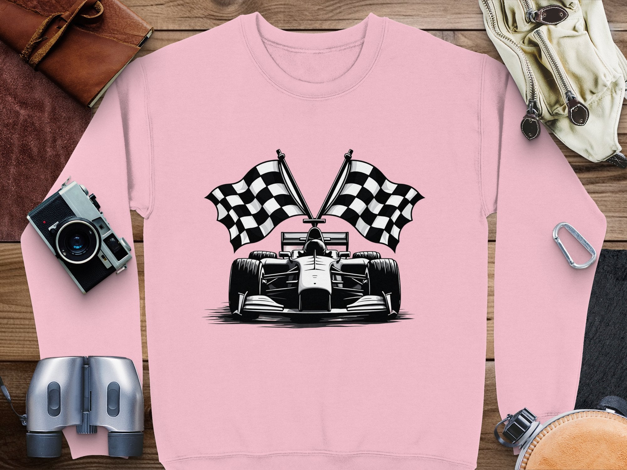 Garment Graphics pink sweatshirt features a racing car with two crossed checkered flags, surrounded by a camera, binoculars, leather gloves, a belt, and sunglasses.