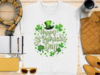The Garment Graphics white T-shirt featuring Happy St. Patricks Day in green, surrounded by shamrocks and a leprechaun hat, adds festive cheer on a wooden surface with accessories like a scarf, pen, notebook, yellow clutch, sunglasses, and coffee nearby.