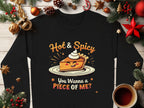 A Garment Graphics black sweatshirt is displayed on wood, featuring a cartoon pie slice with whipped cream, eyes, and a smile. The text reads Hot & Spicy and You Wanna a Piece of Me? It’s surrounded by pine branches, ornaments, and coffee—a versatile unisex piece for any season.