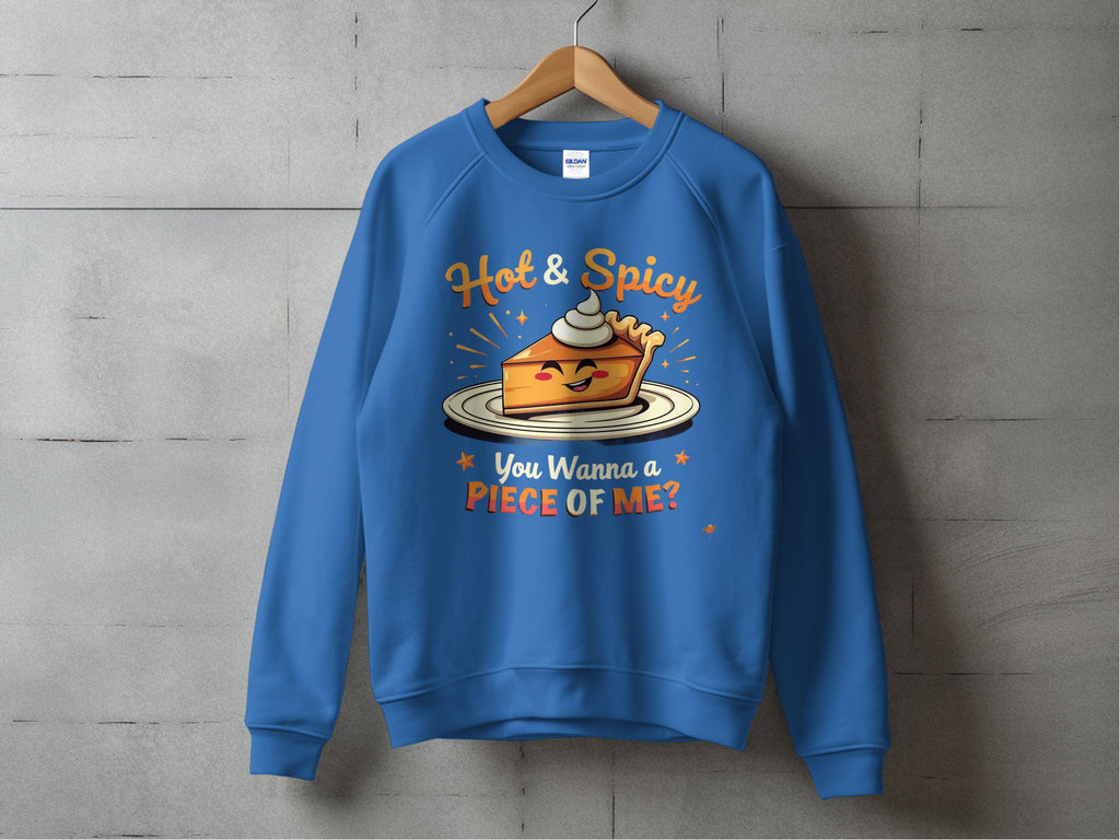 A blue unisex sweatshirt by Garment Graphics hangs on a wooden hanger against a concrete wall, featuring a pie graphic with a mischievous face, cream dollop, and the text Hot & Spicy. You Wanna a Piece of Me? in playful font.