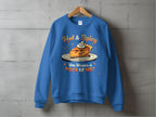 A blue unisex sweatshirt by Garment Graphics hangs on a wooden hanger against a concrete wall, featuring a pie graphic with a mischievous face, cream dollop, and the text Hot & Spicy. You Wanna a Piece of Me? in playful font.
