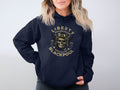 Someone wearing a navy Liberty Motorcycle Specialist Blackpool hoodie from Garment Graphics, featuring a skull with goggles and helmet, strikes a unique look. Their wavy light hair stands out against a neutral backdrop. This hoodie also includes a convenient front pocket.