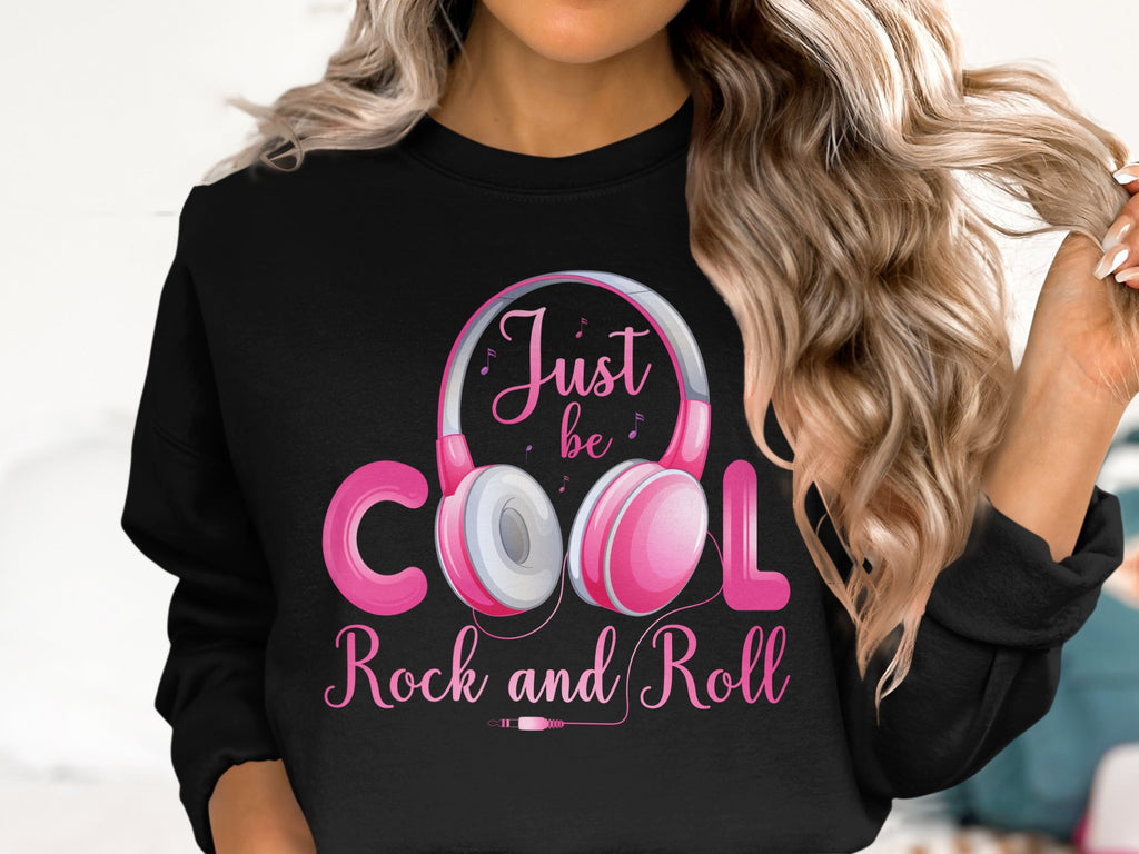 A person with long, wavy hair sports a Garment Graphics black sweatshirt with pink headphones and Just be cool, Rock and Roll text. Ideal for fashion and music lovers, the light backdrop offers subtle contrast.