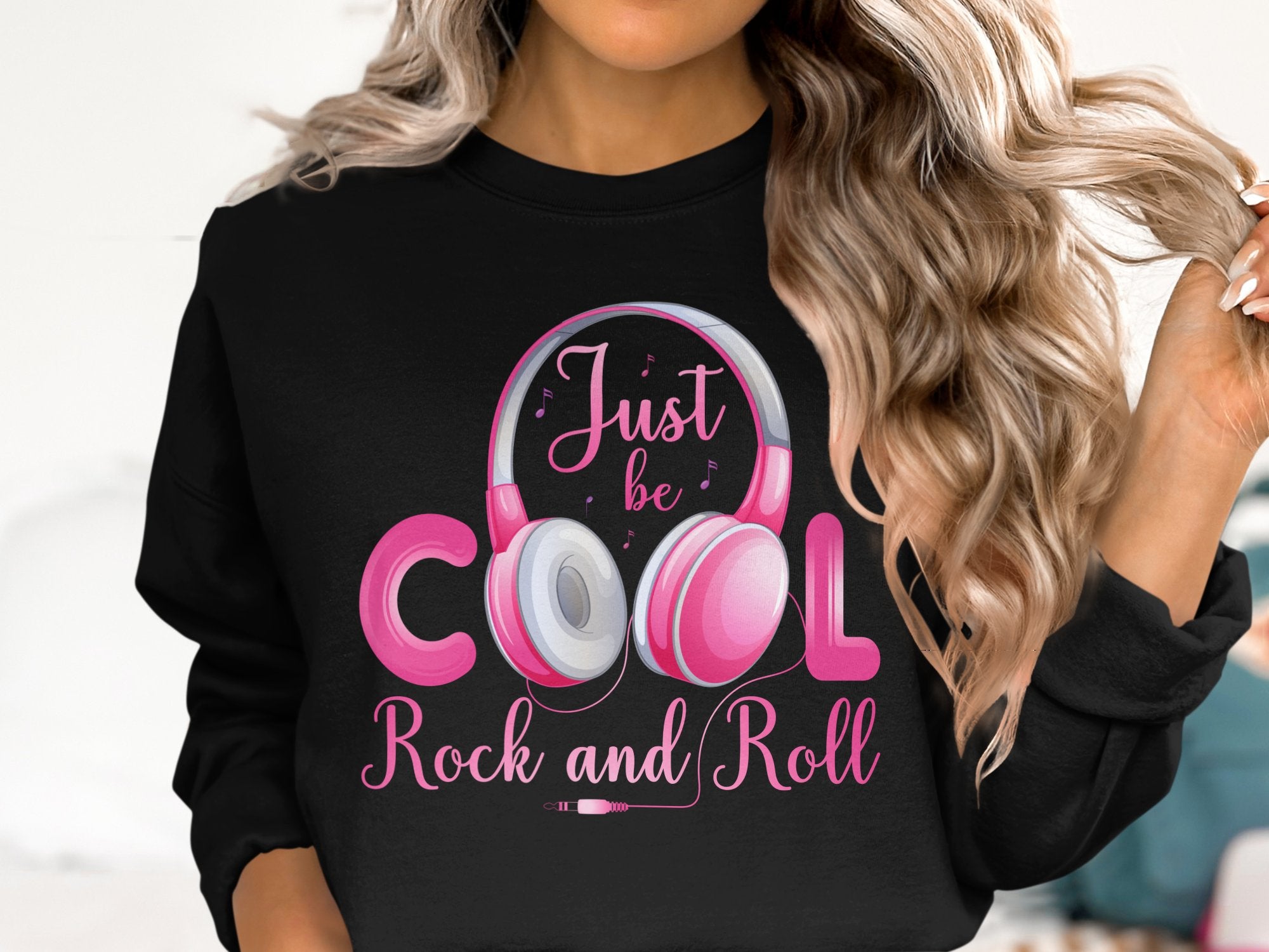 A person with long, wavy hair sports a Garment Graphics black sweatshirt with pink headphones and Just be cool, Rock and Roll text. Ideal for fashion and music lovers, the light backdrop offers subtle contrast.