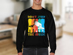 A person is wearing Garment Graphics black DJ sweatshirt, adored by music lovers, featuring a colorful design of a DJ silhouette with turntables and vibrant Dont Stop the Music text on a blurred background.