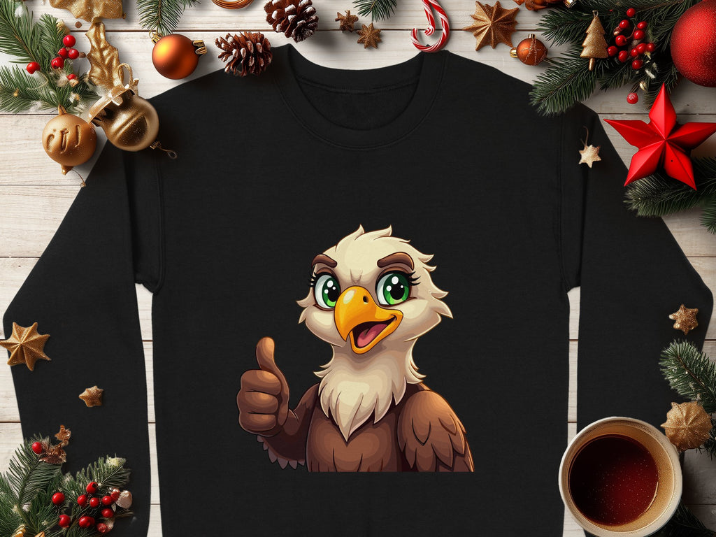 A black shirt from Garment Graphics with a cartoon eagle giving a thumbs-up is laid on wood, surrounded by Christmas decorations like pine branches, pinecones, ornaments, and a cup of dark liquid. The shirt is available in unisex sizes.
