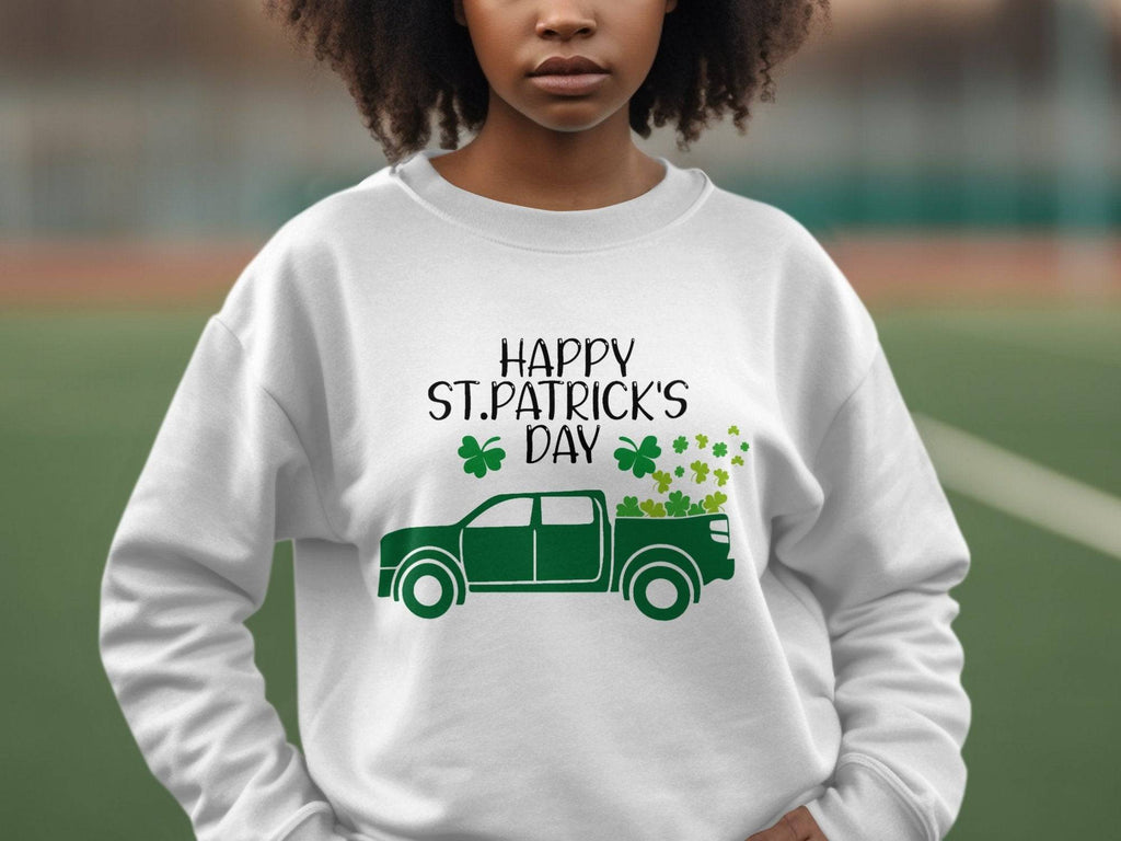 A person proudly wears a Garment Graphics festive sweatshirt showcasing a green truck with shamrocks and Happy St. Patricks Day, standing outdoors, left hand on hip against a blurred background.
