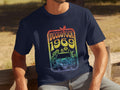 A music lover, wearing a navy blue Garment Graphics T-shirt, sits on a wooden bench. The vibrant design features Woodstock 1969 above a retro van with flowers and a bird.