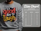 The size chart is for the Garment Graphics Gildan 18000 Heavy Blend Crewneck Sweatshirt, offering unisex sizes S to 5XL with width and length details. A model wears a Graphic Art Sweatshirt reading Its a Good Day to Laugh.