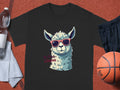 A black Garment Graphics Llama T-shirt displays a cool llama in sunglasses and No Prob-Llama in pink. Styled on red with a water bottle, shorts, towel, and basketball, it offers fun for everyone with family sizing options.