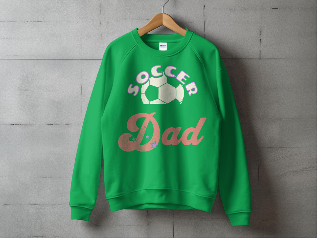 A Garment Graphics unisex Soccer Dad sweatshirt with a soccer ball graphic above the text hangs on a wooden hanger against a concrete wall.