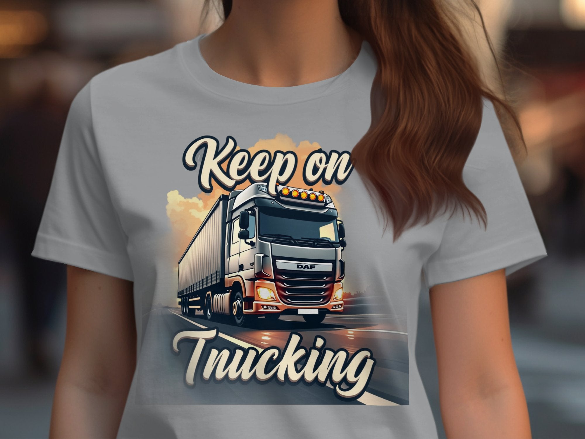 Garment Graphics presents a light gray T-shirt with a bold graphic of a truck under clouds, featuring the text Keep On Trucking. This dynamic design emphasizes the shirt while subtly obscuring the wearers face.
