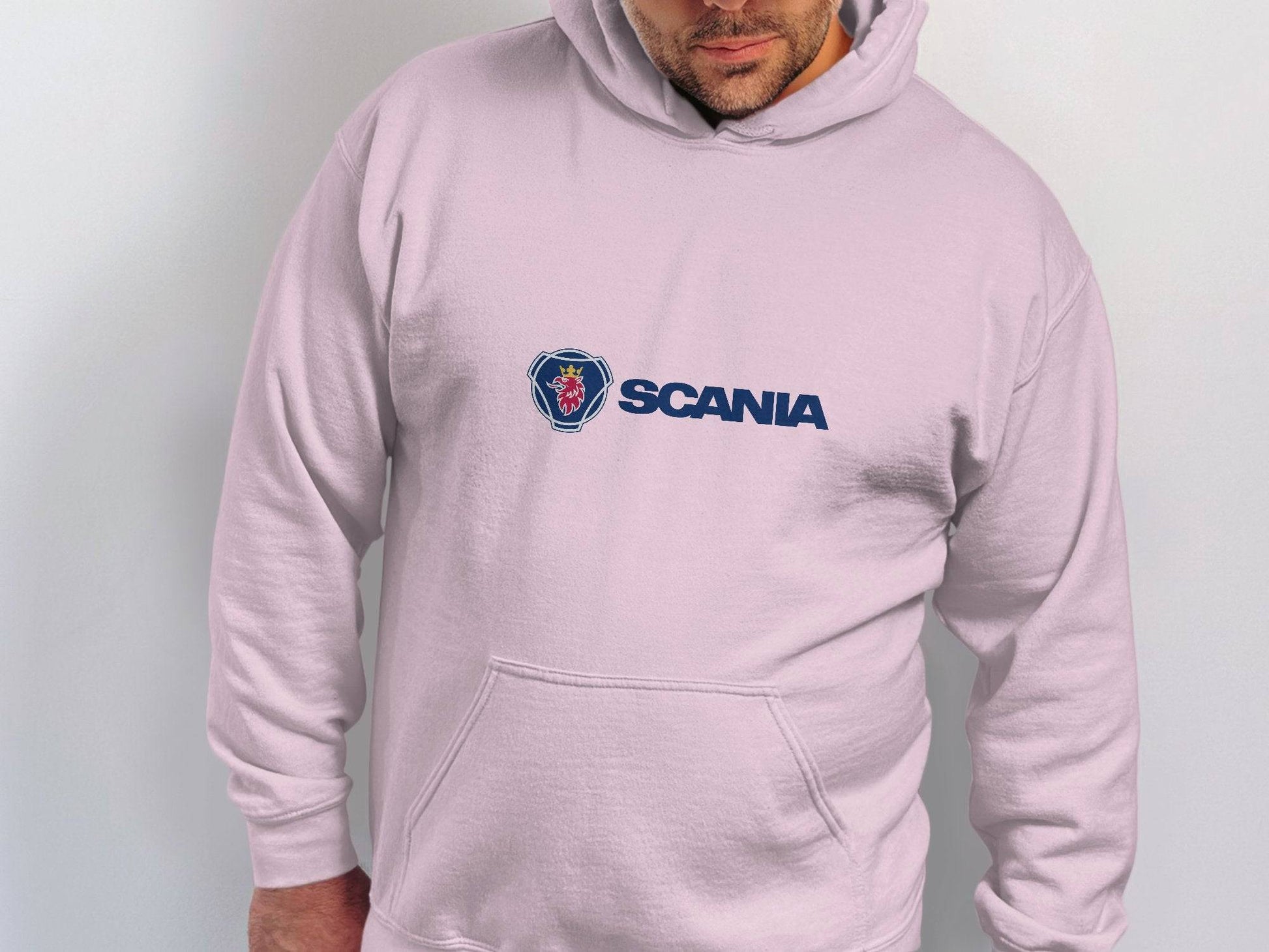 Against a light backdrop, a person dons a white hoodie featuring the iconic Scania logo in blue. This distinctive piece from Garment Graphics captures modern style with its understated yet impactful branding.