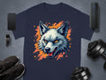A stylish Garment Graphics navy T-shirt with a wolf graphic displaying piercing orange eyes is artfully arranged on a gray surface, surrounded by a smartphone, watch, portable speaker, shoes, and dumbbells.