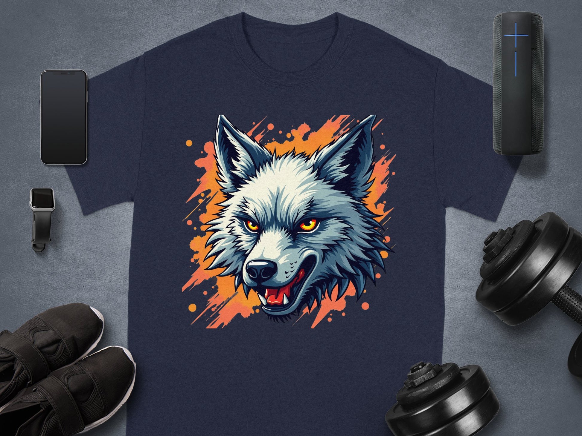 A stylish Garment Graphics navy T-shirt with a wolf graphic displaying piercing orange eyes is artfully arranged on a gray surface, surrounded by a smartphone, watch, portable speaker, shoes, and dumbbells.