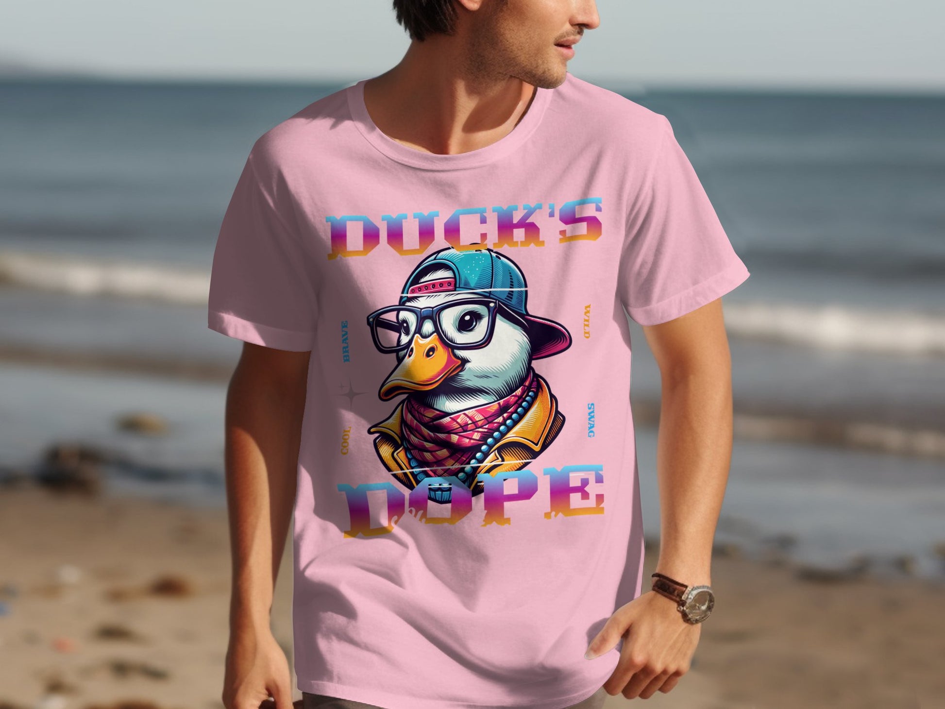 A person walks on the beach in an eye-catching pink Garment Graphics T-shirt with a duck in glasses and a backwards cap. The bold words DUCKS DOPE highlight its unique style against the serene ocean backdrop.