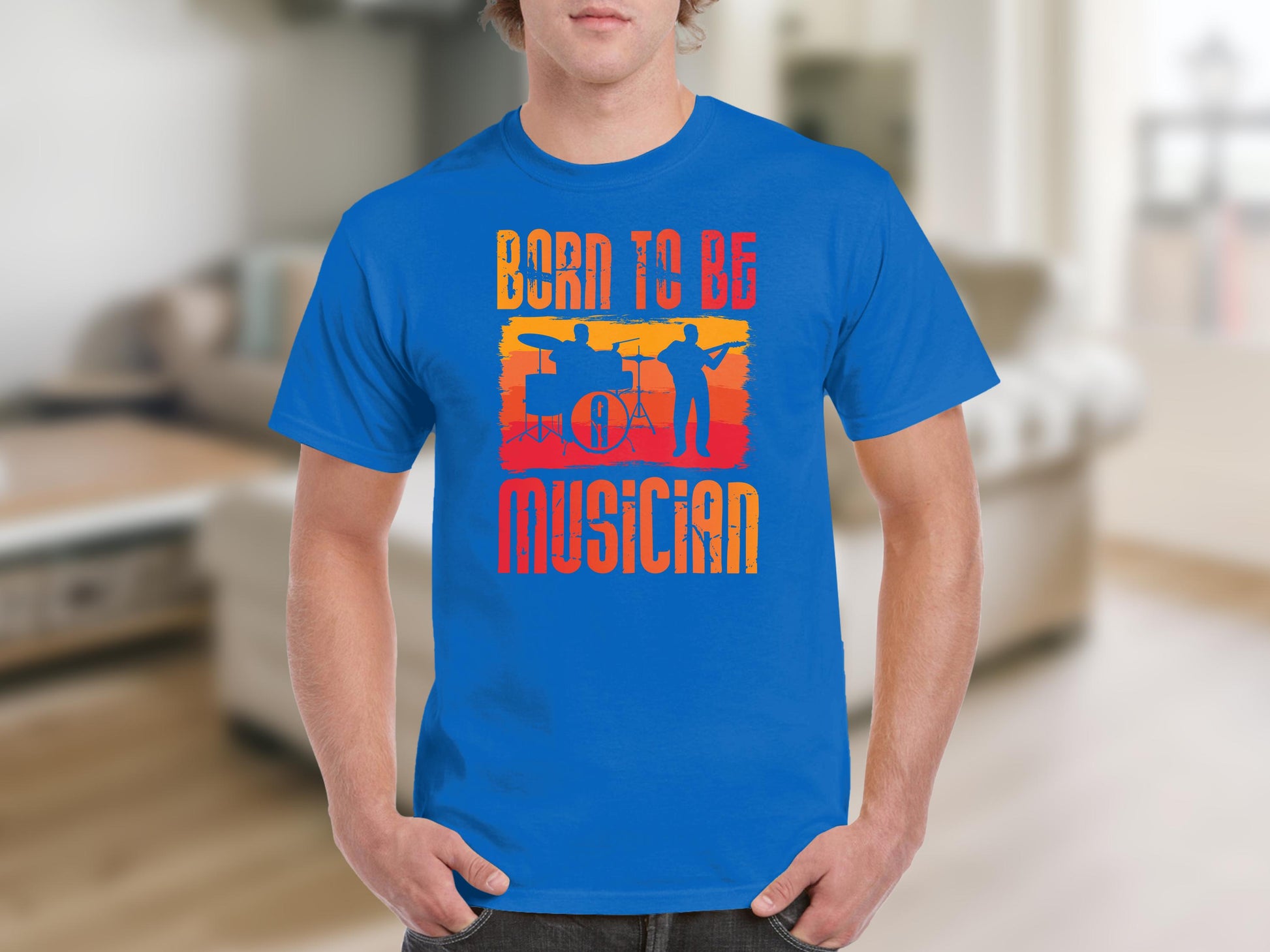 A person in a blue Born To Be Musician T-shirt from Garment Graphics, featuring musician silhouettes like a drummer and guitarist. The design includes bold Born to be a Musician text in an orange-to-yellow gradient, ideal for music enthusiasts.