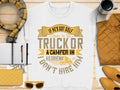 A flat lay showcases a Garment Graphics sweatshirt with If hes got golf clubs in his truck or a camper in his driveway, I dont hire him, alongside a notebook, pen, scarf, sunglasses, quilted bag, tumbler, and quilted jacket.