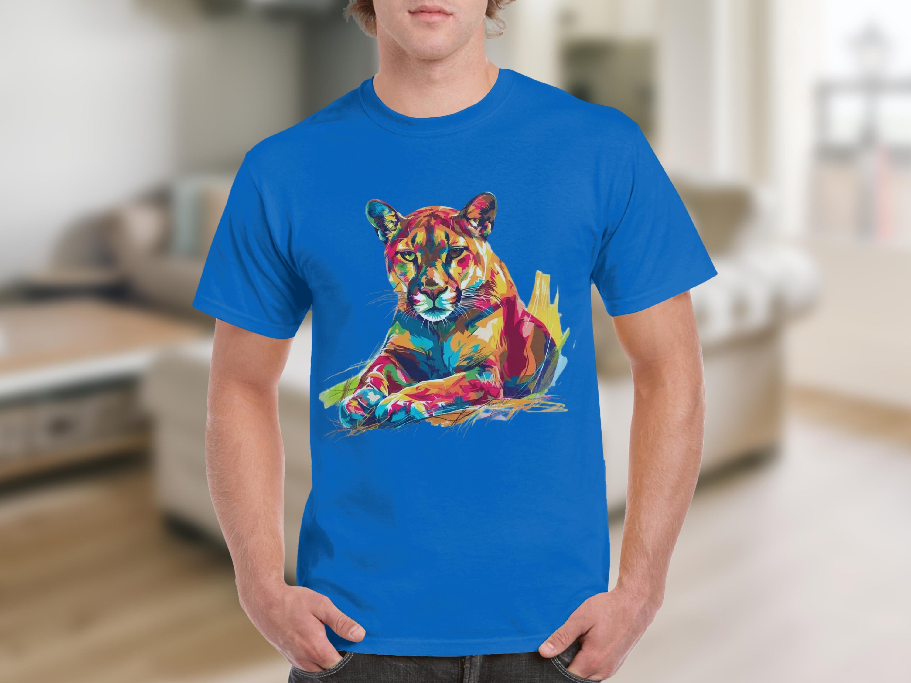 Someone is sporting a Garment Graphics blue graphic print T-shirt showcasing vibrant artwork of a colorful roaring cougar against a softly blurred neutral-toned room with understated furniture.