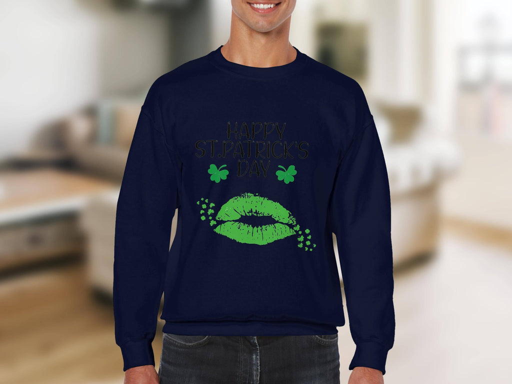 A person is wearing a Garment Graphics dark blue sweatshirt featuring Happy St. Patricks Day in green letters, two shamrocks, and a festive green clover kiss. The background is a blurred indoor setting.