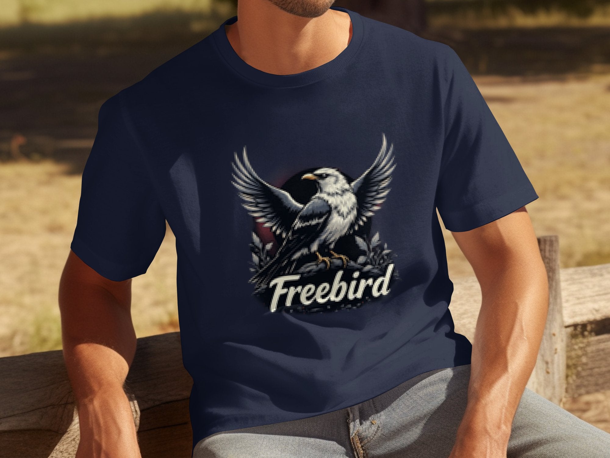 A person in a Garment Graphics Freebird eagle T-shirt, made of 100% cotton adorned with a bold graphic, sits on a wooden bench in a tranquil park.