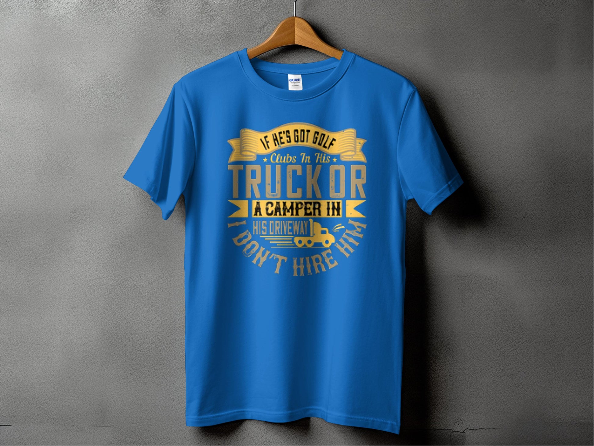 A blue t-shirt by Garment Graphics hangs on a gray wall, featuring the yellow and white text: If hes got golf clubs in his truck or a camper in his driveway, I dont hire him. A small camper graphic complements this witty camping message.