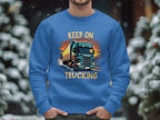 A person in a Garment Graphics sweatshirt with a bold truck design and Keep On Trucking stands against a snowy, out-of-focus tree backdrop, implying a winter scene.