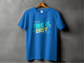 A Garment Graphics Blue T-shirt hangs on a wooden hanger against a gray backdrop, featuring vibrant designs with colorful text and musical notes. The bold TAKE IT EASY phrase makes these Take It Easy T-Shirts perfect for music-inspired fashion lovers.