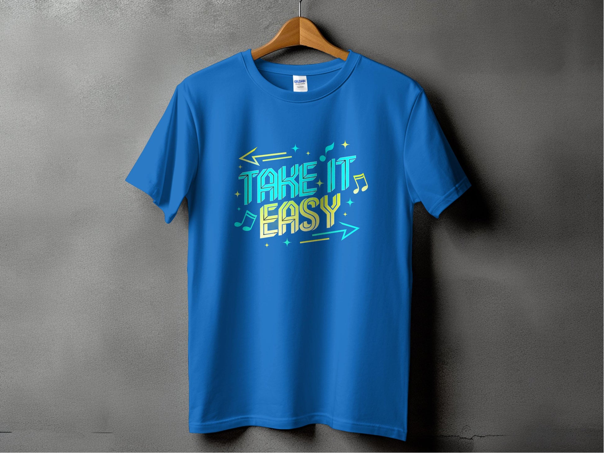 A Garment Graphics Blue T-shirt hangs on a wooden hanger against a gray backdrop, featuring vibrant designs with colorful text and musical notes. The bold TAKE IT EASY phrase makes these Take It Easy T-Shirts perfect for music-inspired fashion lovers.