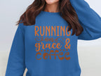 A person is wearing a Garment Graphics blue sweatshirt featuring the phrase Running on Grace and Coffee in orange. Known for its comfy unisex fit, it perfectly complements their long brown hair, though their face isnt visible in the frame.