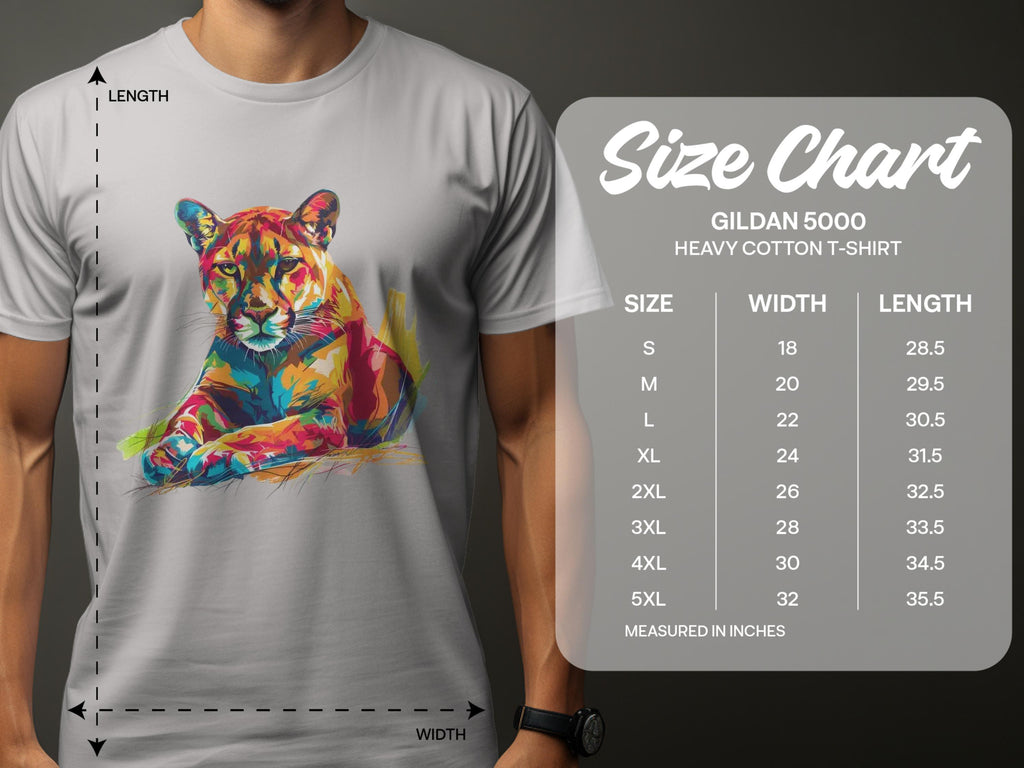 A man wears a light gray Garment Graphics T-shirt featuring a colorful roaring cougar design. Next to him is the size chart for the Gildan 5000 heavy cotton T-shirt, listing sizes S to 5XL with corresponding width and length measurements in inches.