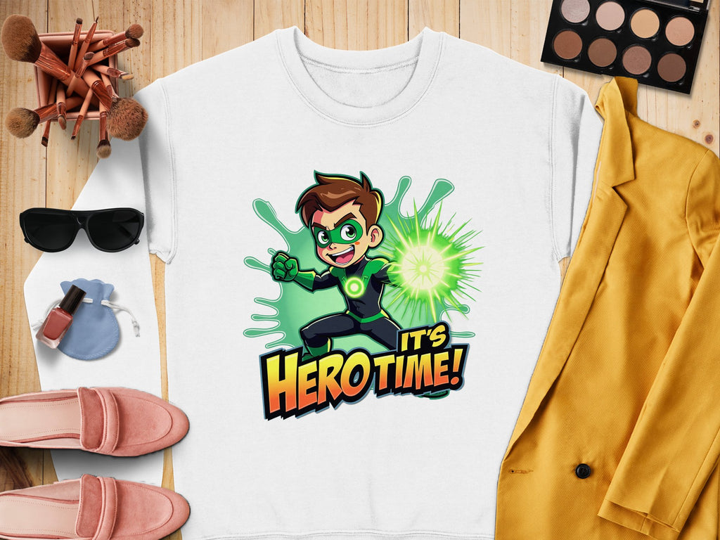Garment Graphics offers a white unisex cartoon-themed sweatshirt showcasing a superhero with brown hair and a green glowing fist, alongside the text Its Hero Time! The scene includes makeup, sunglasses, pink shoes, a yellow jacket, and a small pouch on wood.