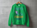 A green graphic sweatshirt by Garment Graphics hangs on a wooden hanger against a concrete wall. It features Daddys Fishing Buddy with a fish and fishing boat silhouette, perfect for outdoor enthusiasts celebrating the great outdoors.