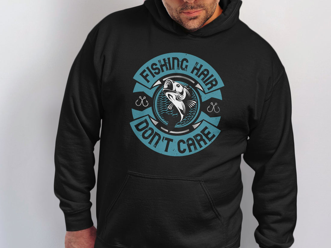 A man sports a Garment Graphics black hoodie with a vibrant fish design, featuring Fishing Hair Dont Care in teal and white letters and small fishhook illustrations, making it perfect for any angler.