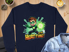Navy blue sweatshirt by Garment Graphics with a cartoon superhero boy holding a glowing green object and Its Hero Time! print. It sits on a wooden table with a denim jacket, heart latte, and decorative stones nearby. Unisex sizes available!.